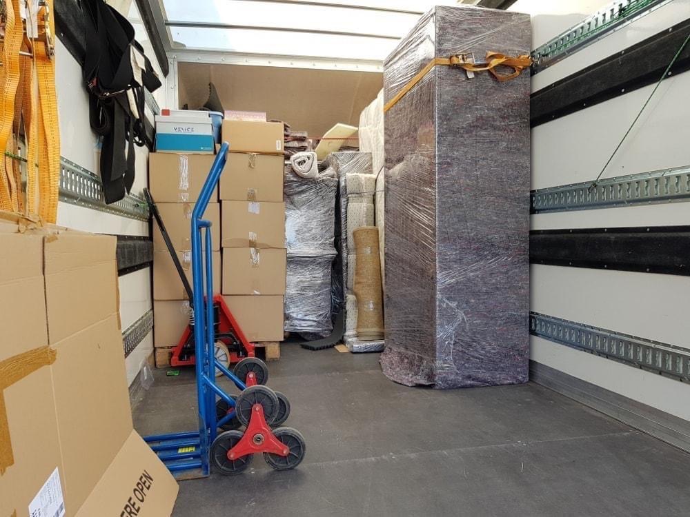 Wnętrze busa załadowane kartonami, meblami owiniętymi folią stretch i wózkiem transportowym z trójkołowymi gwiazdami na schody.