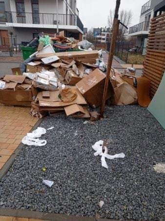 Stos kartonów, gruzu i innych odpadów po remoncie leży na kostce brukowej i żwirze na zewnątrz budynku mieszkalnego.
