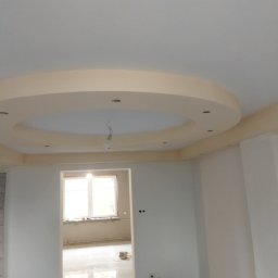 Budownictwo - Wnętrze pokoju po remoncie z dekoracyjnym okrągłym podwieszanym sufitem z punktowym oświetleniem, widoczne ślady prac wykończeniowych na podłodze i wiaderka z farbą.