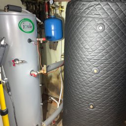 WAGREX bis Sebastian Piątkowski - Dwa zbiorniki akumulacyjne ciepła: szary z logo Joule i czarny z pikowaną izolacją, połączone instalacją hydrauliczną w pomieszczeniu technicznym.