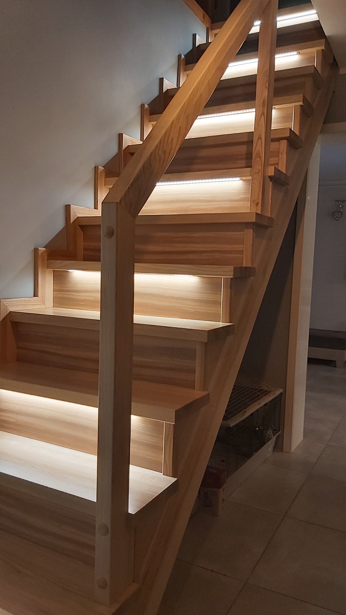 Drewniane schody z podświetleniem LED pod każdym stopniem, widok z dołu, jasne drewno, minimalistyczny design.