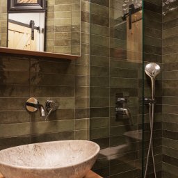 Knyf Studio - Nowoczesna łazienka z umywalką z kamienia, zielonymi płytkami i kabiną prysznicową ze szklaną ścianką, odbicie drewnianych drzwi w szkle.