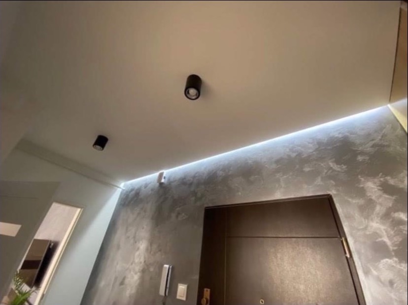 Nowoczesne wykończenie wnętrza: ściana z efektem dekoracyjnym, oświetlenie LED i czarne lampy sufitowe. Minimalistyczny design, widok z dołu.