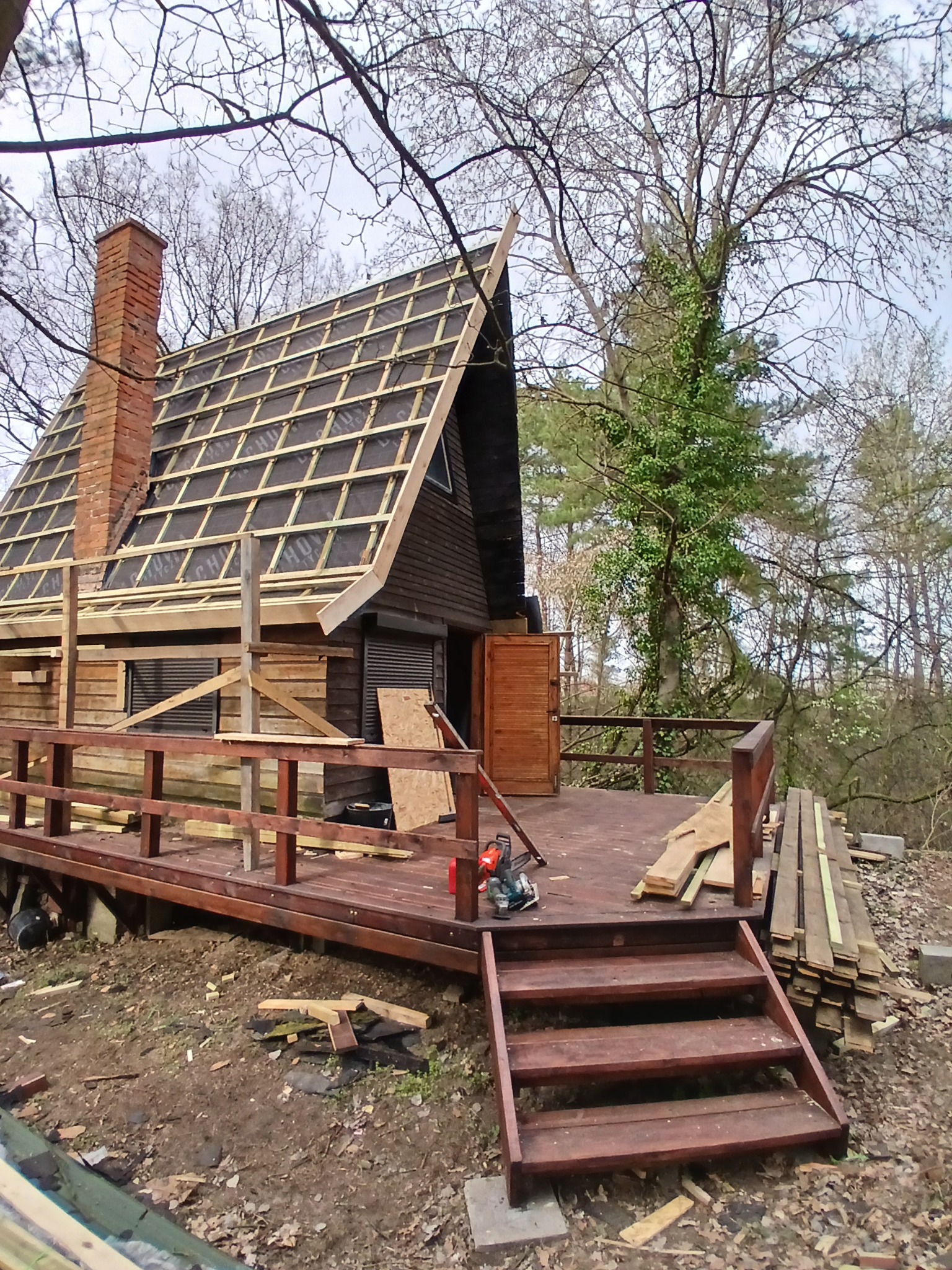 Budowa drewnianego domu z tarasem: widoczny etap montażu dachu i konstrukcji tarasu z balustradą. Na pierwszym planie schody i stos desek.