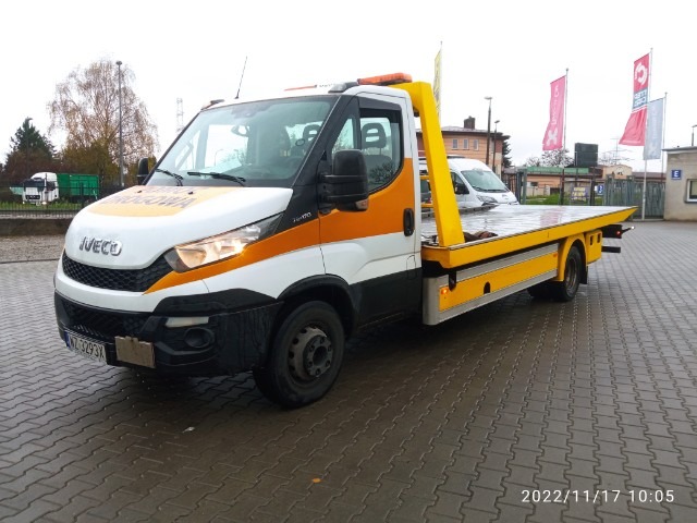 Biało-żółta laweta Iveco z napisem 'Pomoc Drogowa' na tle szarej kostki brukowej i budynków w tle, z widoczną datą i godziną na dole zdjęcia.