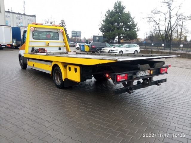 Żółto-biała platforma pojazdu pomocy drogowej z wysuniętą platformą, widok z tyłu na mokrym brukowanym placu, tablica rejestracyjna WZ 3293X.