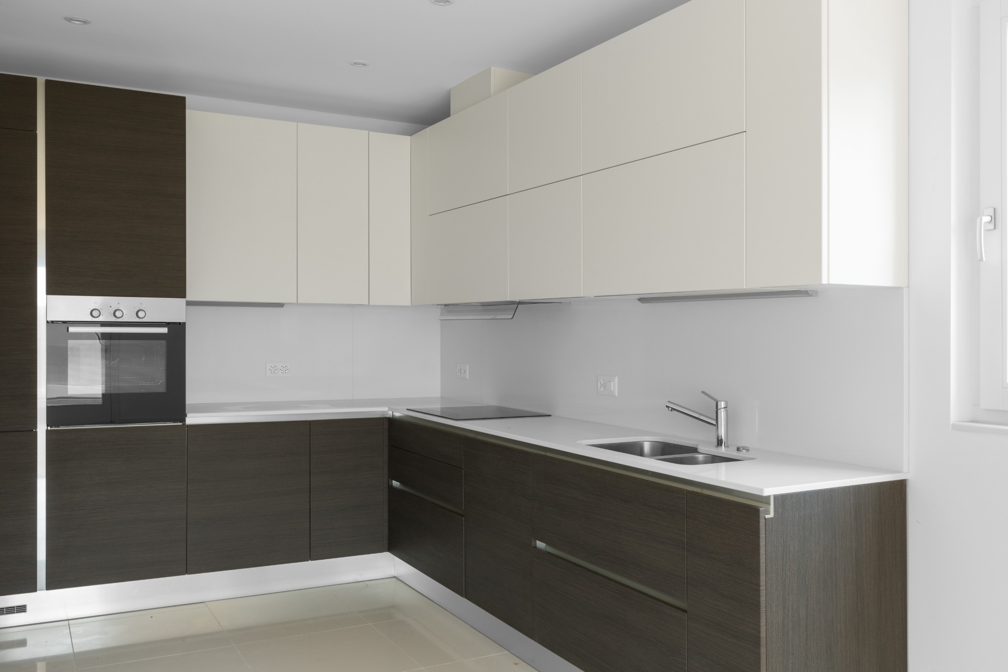 Nowoczesna kuchnia z dwukolorowymi frontami szafek w Żurominie: ciemnobrązowe drewno na dole i kremowa biel na górze, z wbudowanym piekarnikiem i minimalistycznym zlewem.