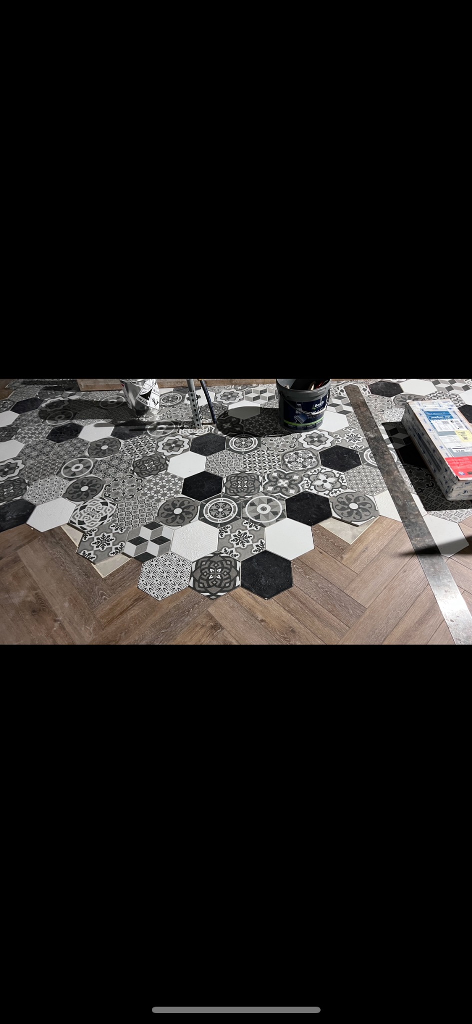 Ukończona podłoga z heksagonalnych płytek w odcieniach szarości i bieli, ułożonych na parkiecie w jodełkę. Widoczne narzędzia i puszka farby.
