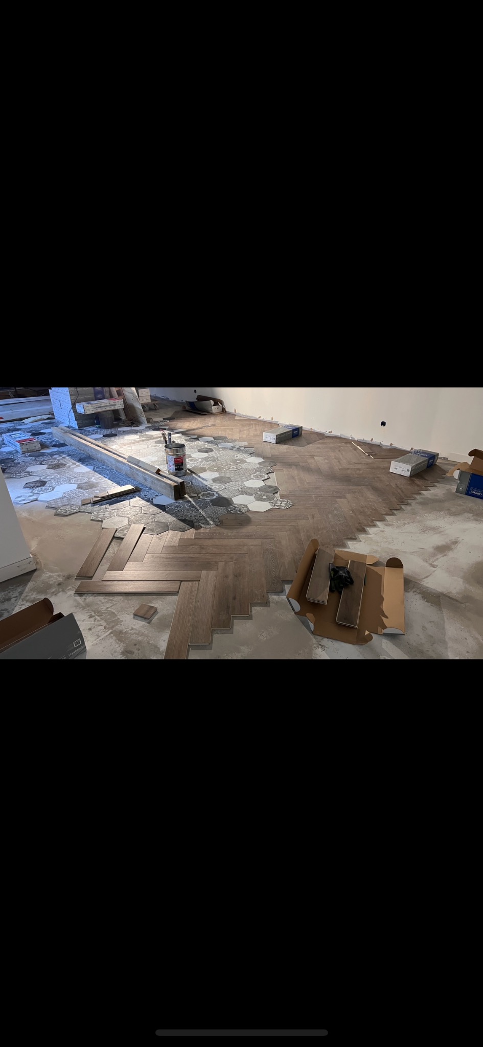 Fragment układania podłogi z drewnopodobnych paneli w jodełkę, widoczne narzędzia, częściowo ułożona podłoga i materiały wykończeniowe.