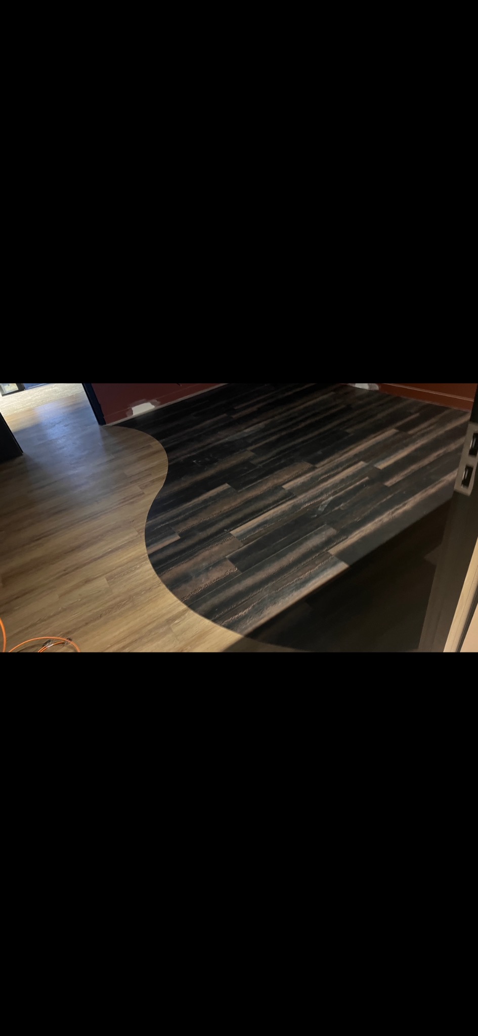 Układanie dwukolorowych paneli podłogowych w kształcie fali, widok z góry, kontrast jasnego i ciemnego drewna, częściowo widoczny kabel elektryczny.