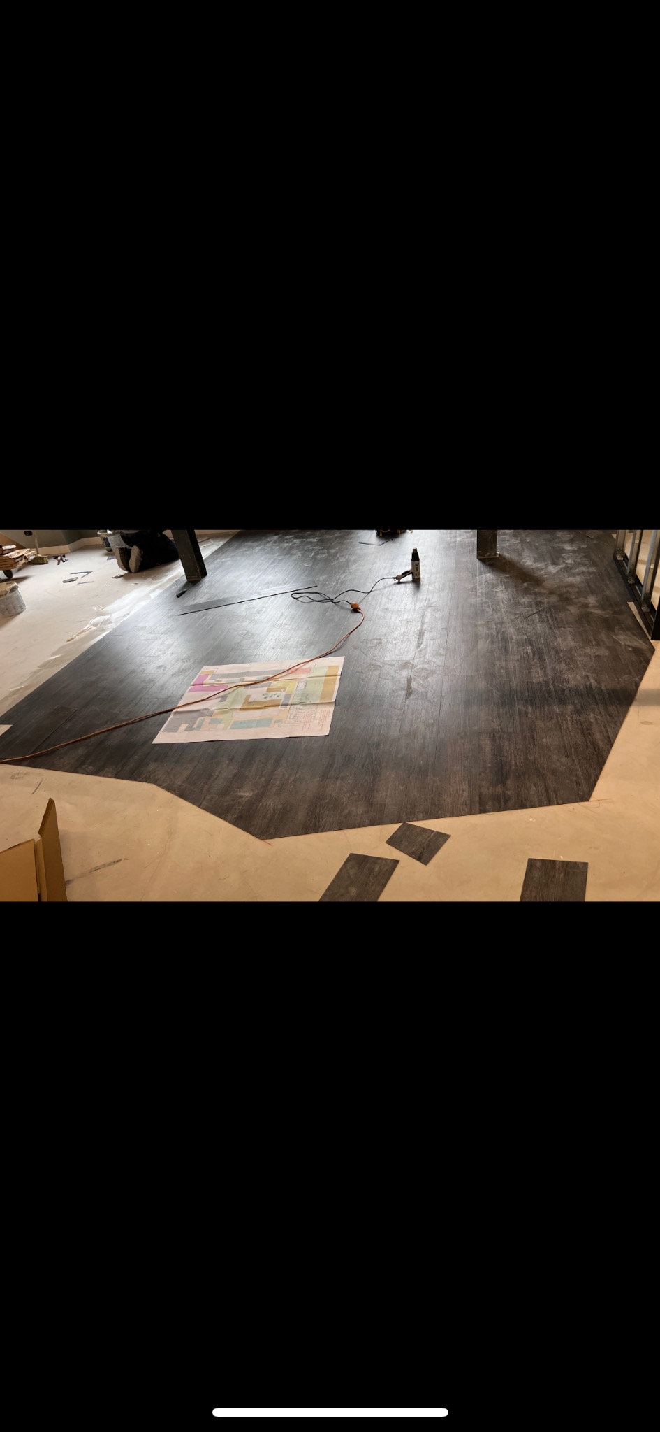 Układanie paneli winylowych w pomieszczeniu. Widoczny plan pomieszczenia, narzędzia i panele w odcieniach brązu. Część podłogi jest już pokryta panelami.