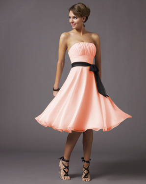 Krótka, brzoskwiniowa sukienka bez ramiączek z czarną szarfą w talii, obracająca się na modelce na szarym tle, z widocznymi sandałami na wysokim obcasie.