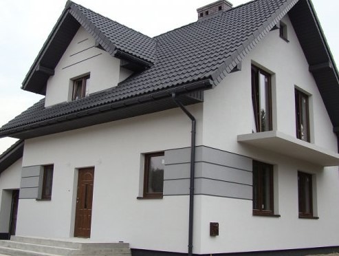 Dwukondygnacyjny dom z białą elewacją, ciemną dachówką i szarymi pasami dekoracyjnymi, widok z dołu.