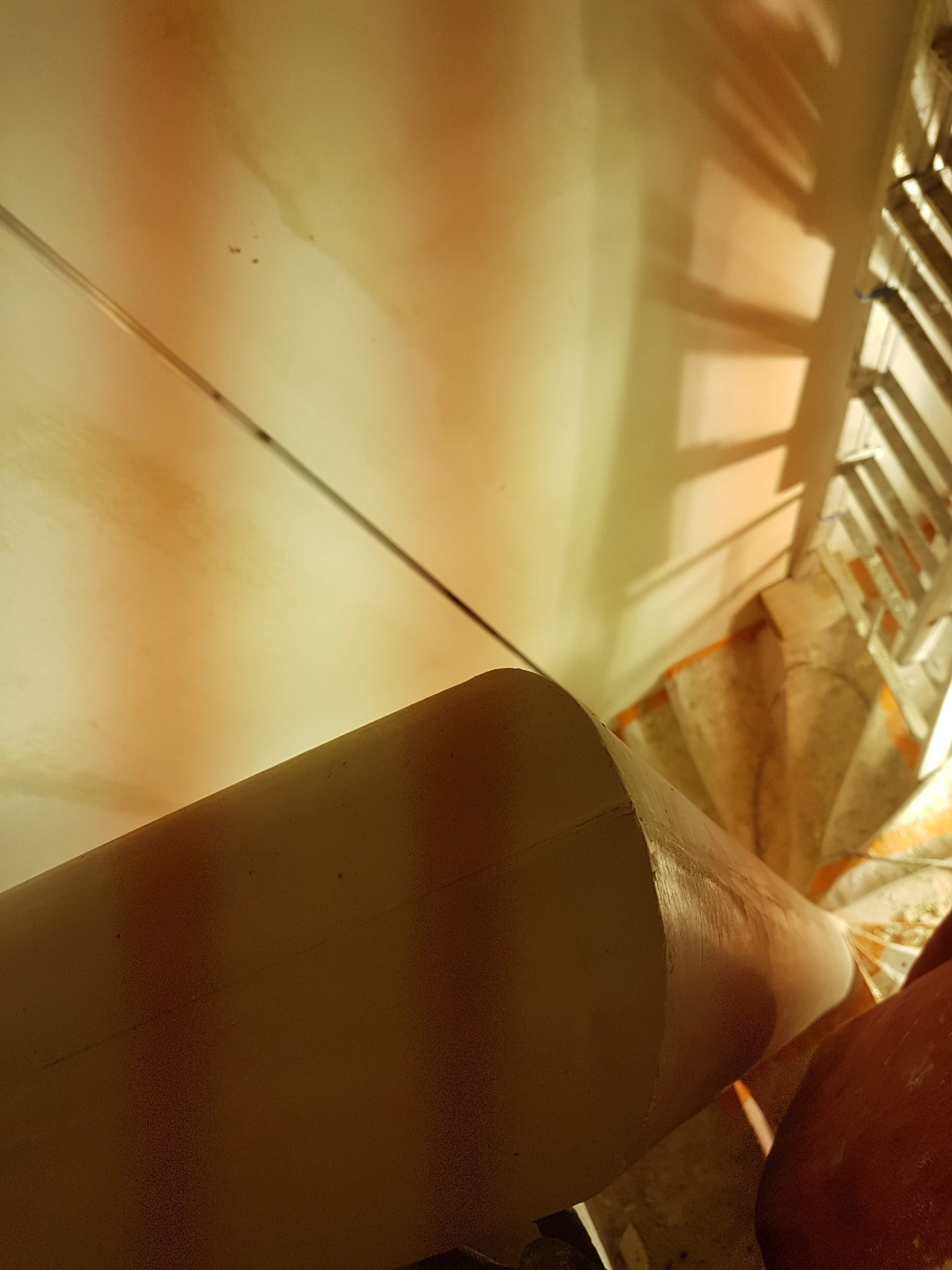 Wnętrze klatki schodowej w trakcie prac wykończeniowych; widoczna obłożona folią ochronną spiralna balustrada i schody, oraz ściana w trakcie wyrównywania pod kątem, z widocznym oświetleniem roboczym.