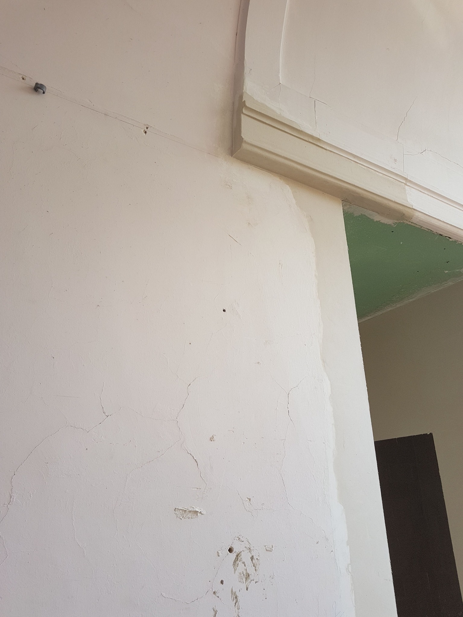 Fragment ściany z widocznymi pęknięciami i fragmentem szpachlowania przy ościeżnicy, sufit w kolorze zielonym.