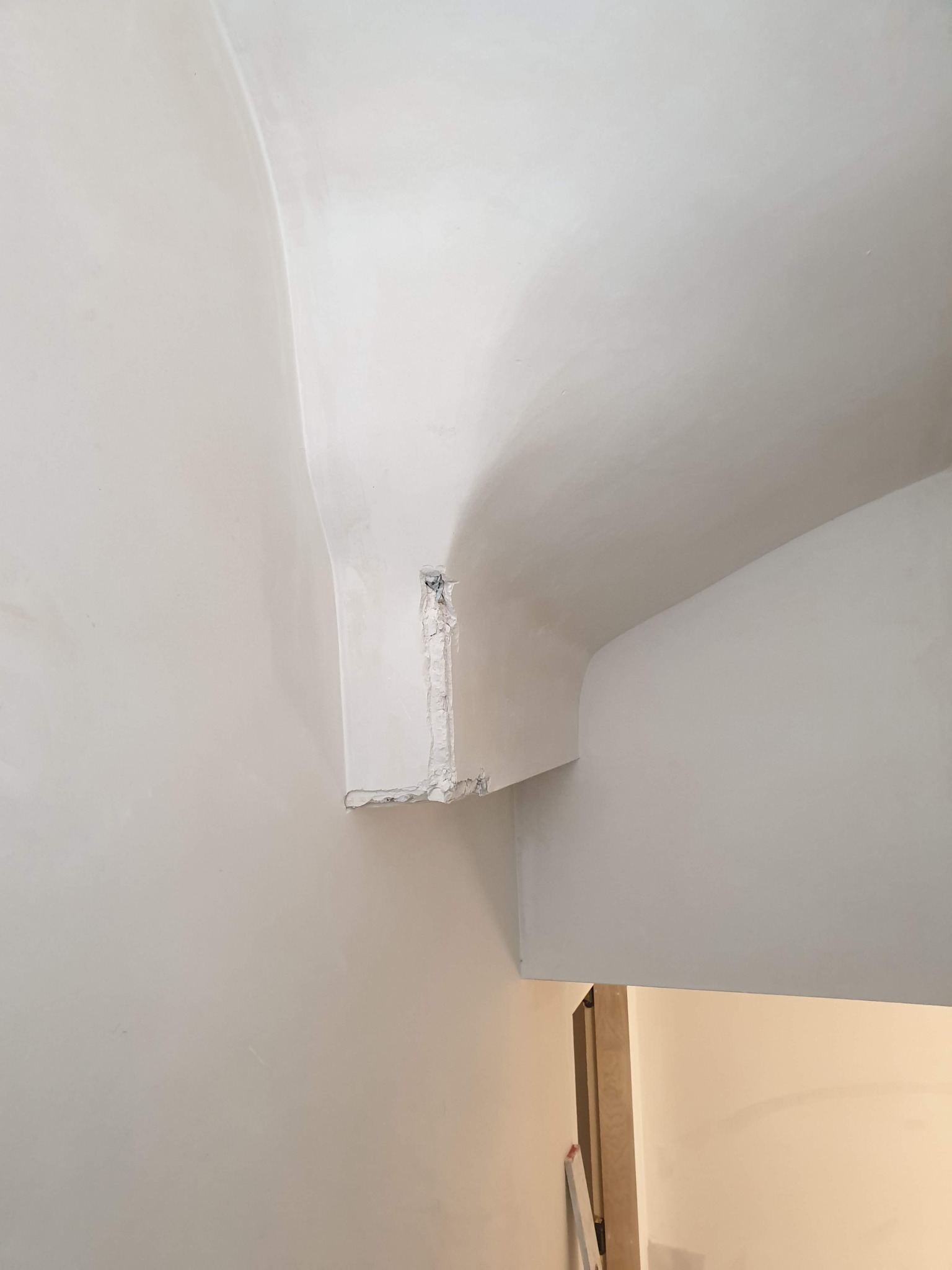 Fragment ściany i sufitu z widocznym niedokończonym narożnikiem, odsłaniającym warstwy materiału budowlanego przed nałożeniem gładzi.