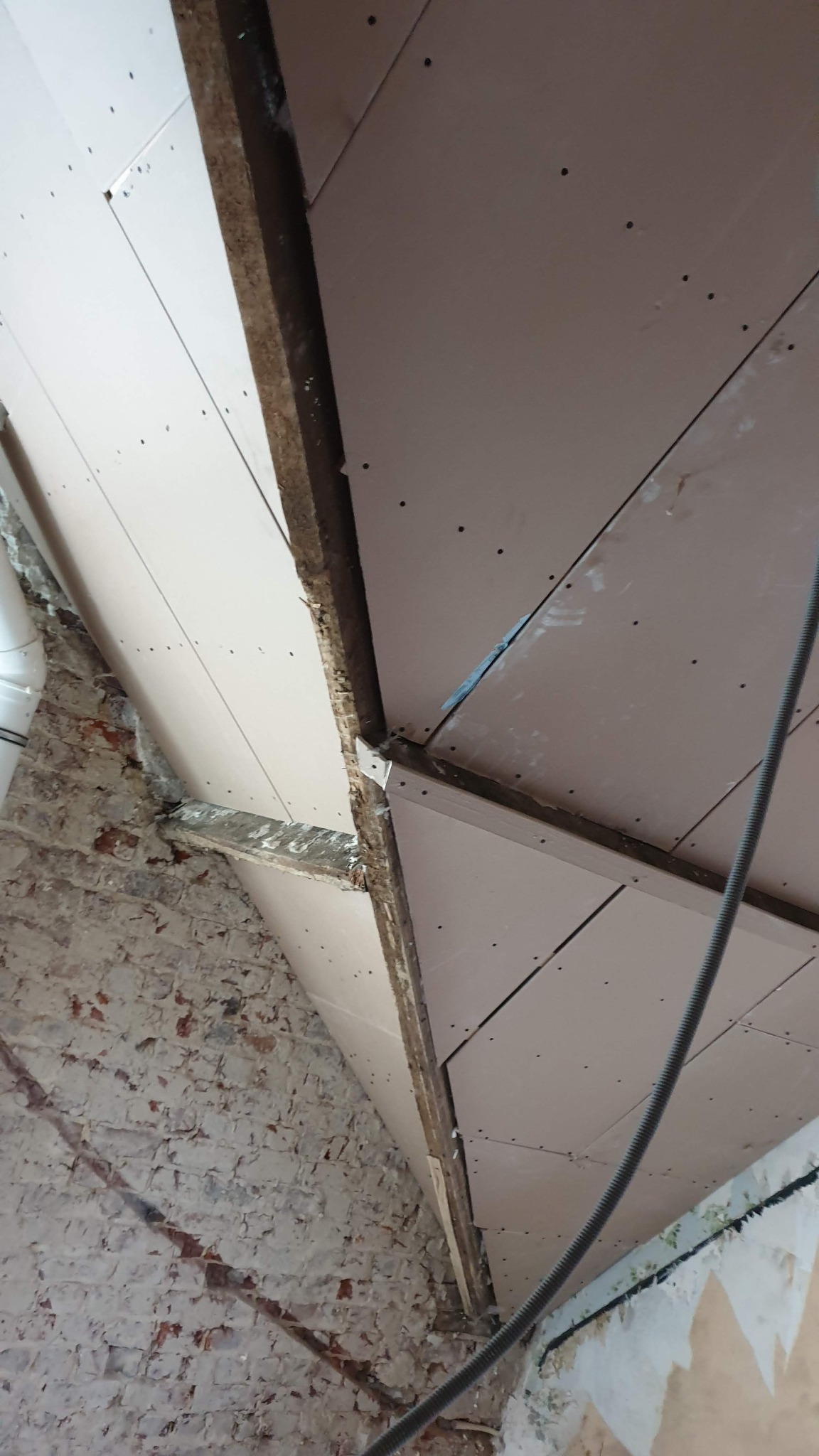 Sufit z płyt gipsowo-kartonowych zamontowanych na drewnianej konstrukcji, widoczne ślady po wkrętach, fragment ściany z cegły i instalacja elektryczna.