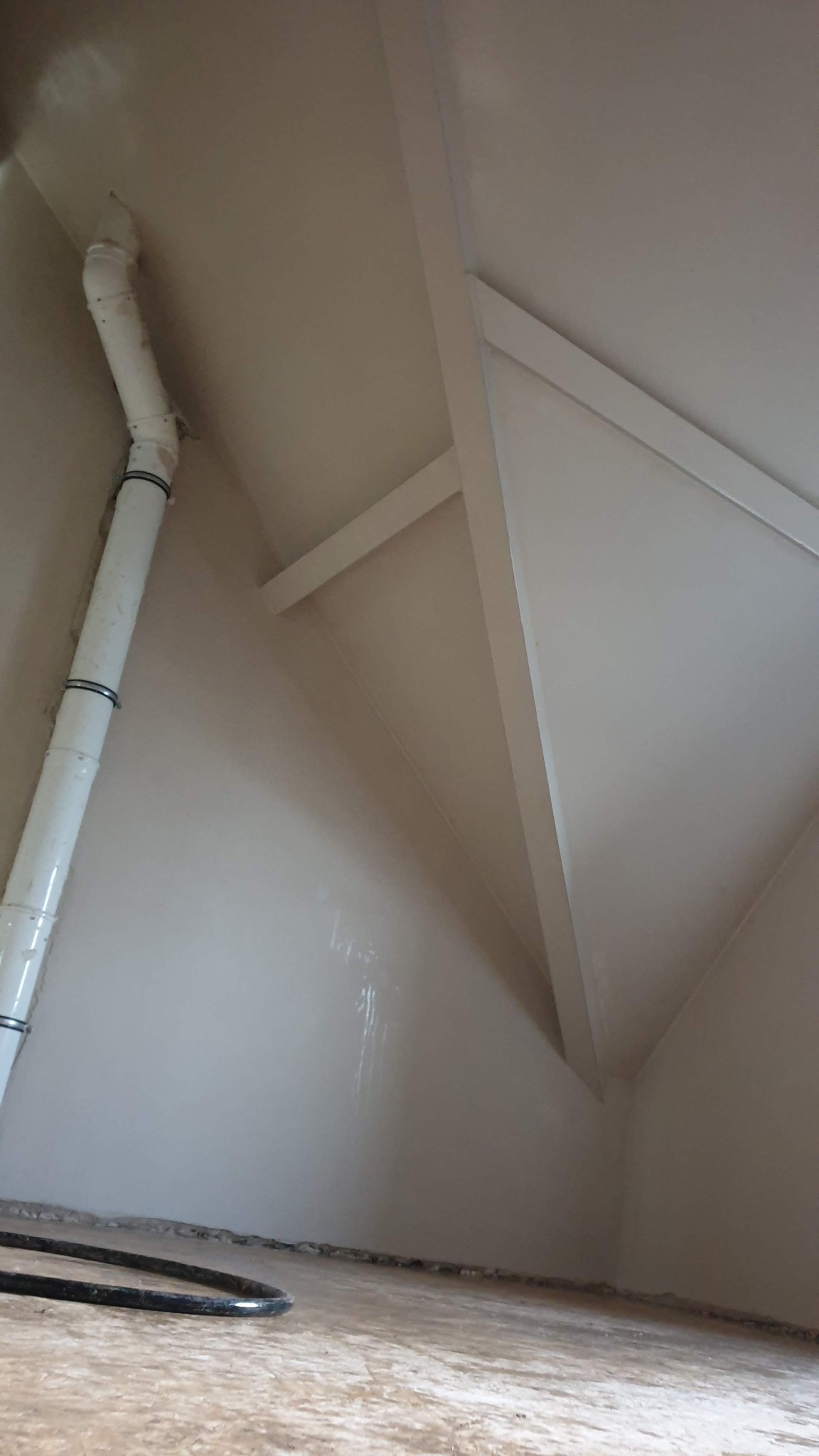 Świeżo wykończone poddasze z gładkimi, jasnymi ścianami i widoczną rurą wentylacyjną z czarnymi opaskami, ukazujące efekt pracy wykończeniowej.