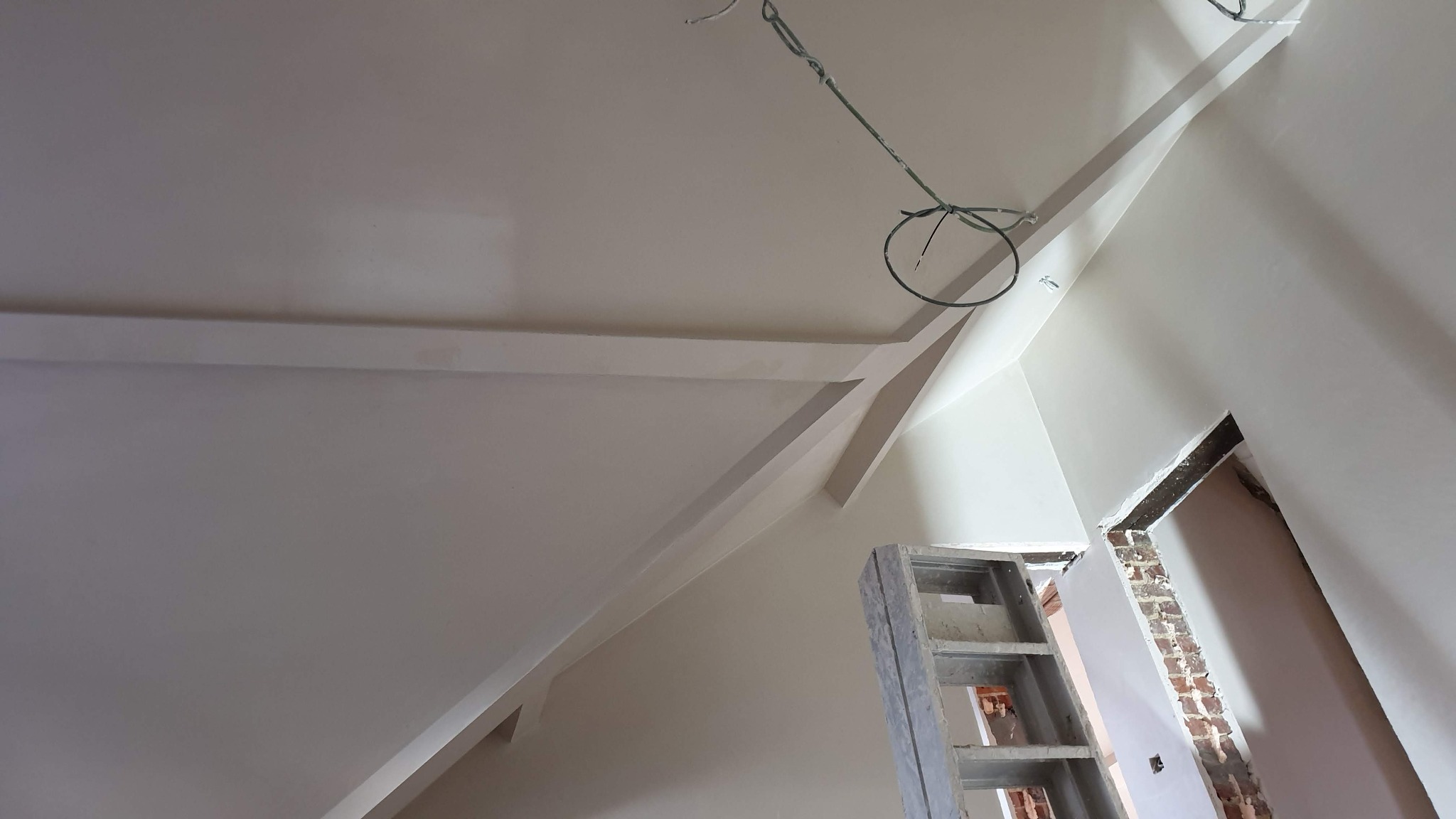 Poddasze po zakończonym szpachlowaniu i malowaniu, widoczne gładkie ściany ze skosami, fragment drabiny i wystające przewody elektryczne.