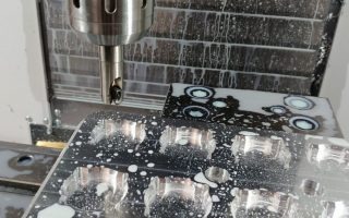 Frezarka numeryczna w trakcie obróbki metalowego elementu. Wióry i chłodziwo widoczne na powierzchni obrabianego przedmiotu i w otoczeniu maszyny. Widoczne detale frezu i uchwytu narzędziowego.