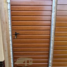 Zamknięta, brązowa brama garażowa segmentowa z widocznymi uszczelnieniami pianką montażową i logo firmy BramDex Stal na dole.