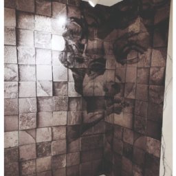 NICE NICE DESIGN - Ściana łazienki pokryta tapetą z efektem 3D kostek w odcieniach brązu i szarości, tworzących portret twarzy; biała marmurowa podłoga i minimalistyczne oświetlenie sufitowe.