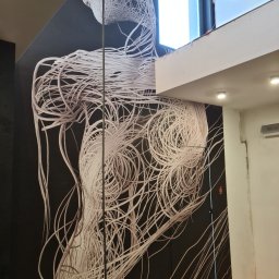 NICE NICE DESIGN - Abstrakcyjna fototapeta z motywem splątanych białych kabli na czarnym tle, widoczna na ścianie w trakcie wykańczania wnętrza, z fragmentem okna i sufitu