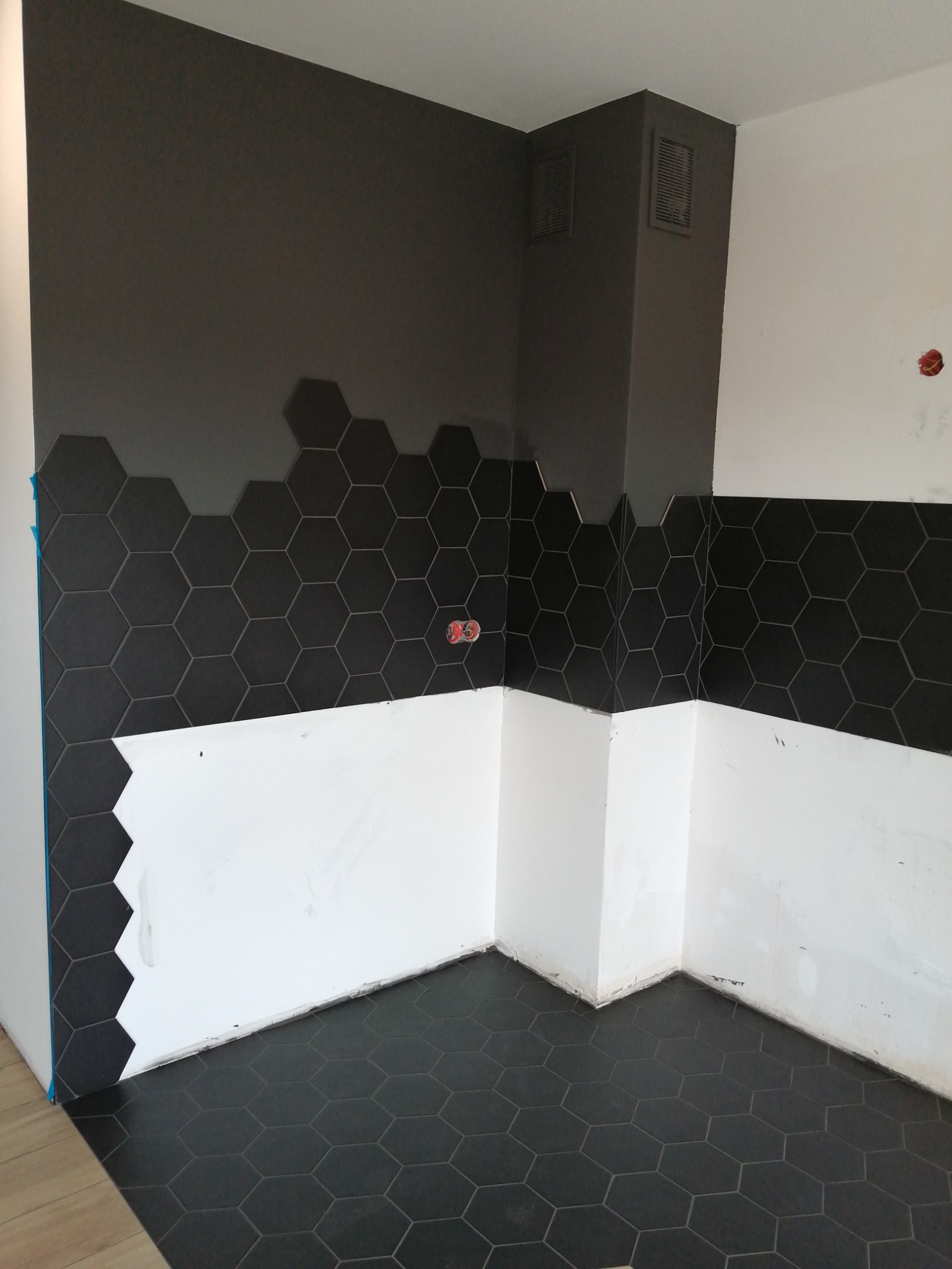 Układanie heksagonalnych, czarnych płytek na ścianie i podłodze w trakcie remontu łazienki w Stargardzie; widoczne niedokończone białe fragmenty ścian.