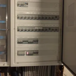 Otwarta skrzynka rozdzielcza z bezpiecznikami i licznymi przewodami elektrycznymi w ścianie w trakcie instalacji, Warszawa.