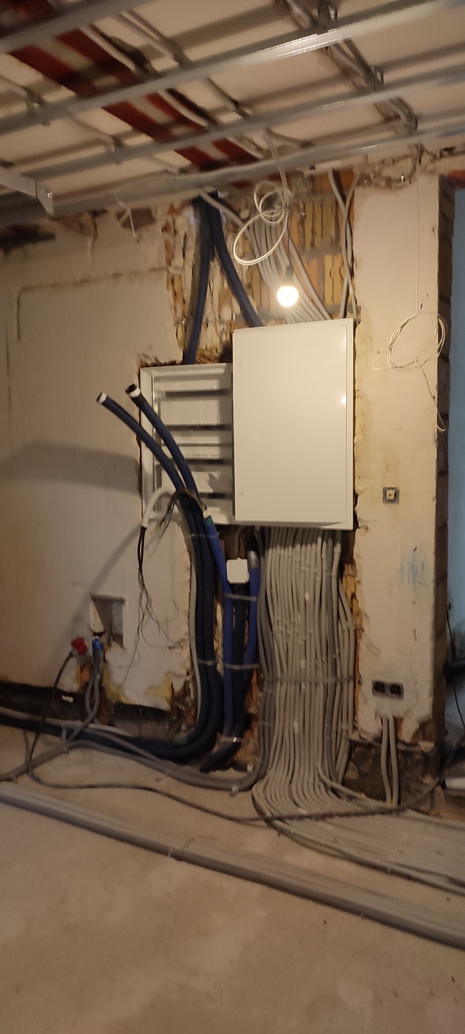 Wewnętrzna instalacja elektryczna w trakcie montażu: biała skrzynka rozdzielcza, liczne kable w peszlach, surowy stan ścian i sufitu podwieszanego.