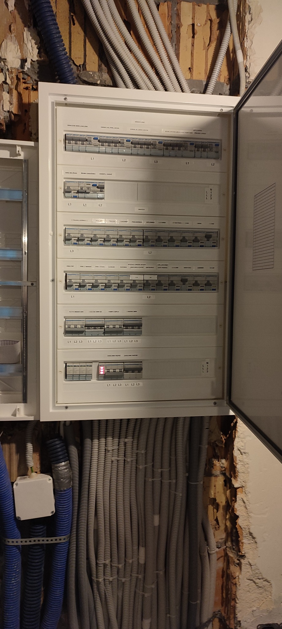Otwarta skrzynka rozdzielcza z bezpiecznikami i licznymi przewodami elektrycznymi w ścianie w trakcie instalacji, Warszawa.