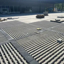 Układanie ażurowej kostki brukowej w geometryczny wzór na placu. Widoczne palety z kostką i częściowo ułożone fragmenty nawierzchni. Nowoczesny design.