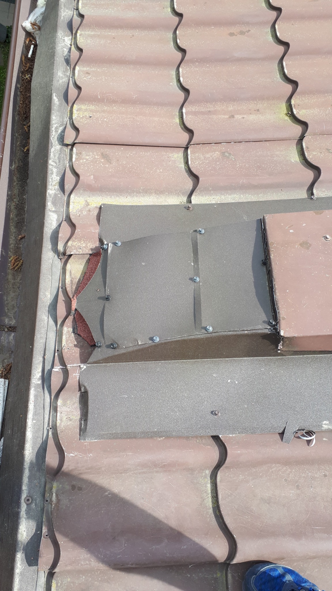 Szczegółowe ujęcie fragmentu brązowego dachu z zamontowanymi szarymi elementami blacharskimi, zabezpieczonymi śrubami, widoczne ślady wcześniejszych prac dekarskich.