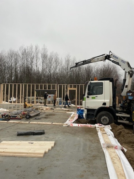 Montaż szkieletu budynku z użyciem dźwigu samochodowego, widoczne elementy konstrukcyjne i ekipa budowlana na placu budowy.