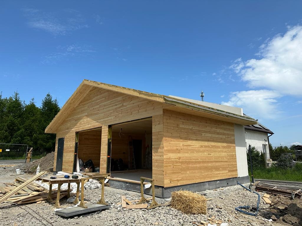 Konstrukcja budynku w trakcie budowy z drewnianą elewacją, widoczne przygotowane deski i narzędzia na zewnątrz.