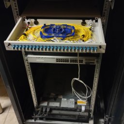 BTELCO - Szafa rack Legrand z wysuwaną półką zawierającą patch panel światłowodowy z żółtymi kablami światłowodowymi i niebieską kasetą spawów.