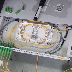 BTELCO - Rozdzielnica światłowodowa z uporządkowanymi kablami światłowodowymi wewnątrz, widoczne złącza SC/APC w kolorze zielonym i narzędzie do czyszczenia światłowodów na górze.