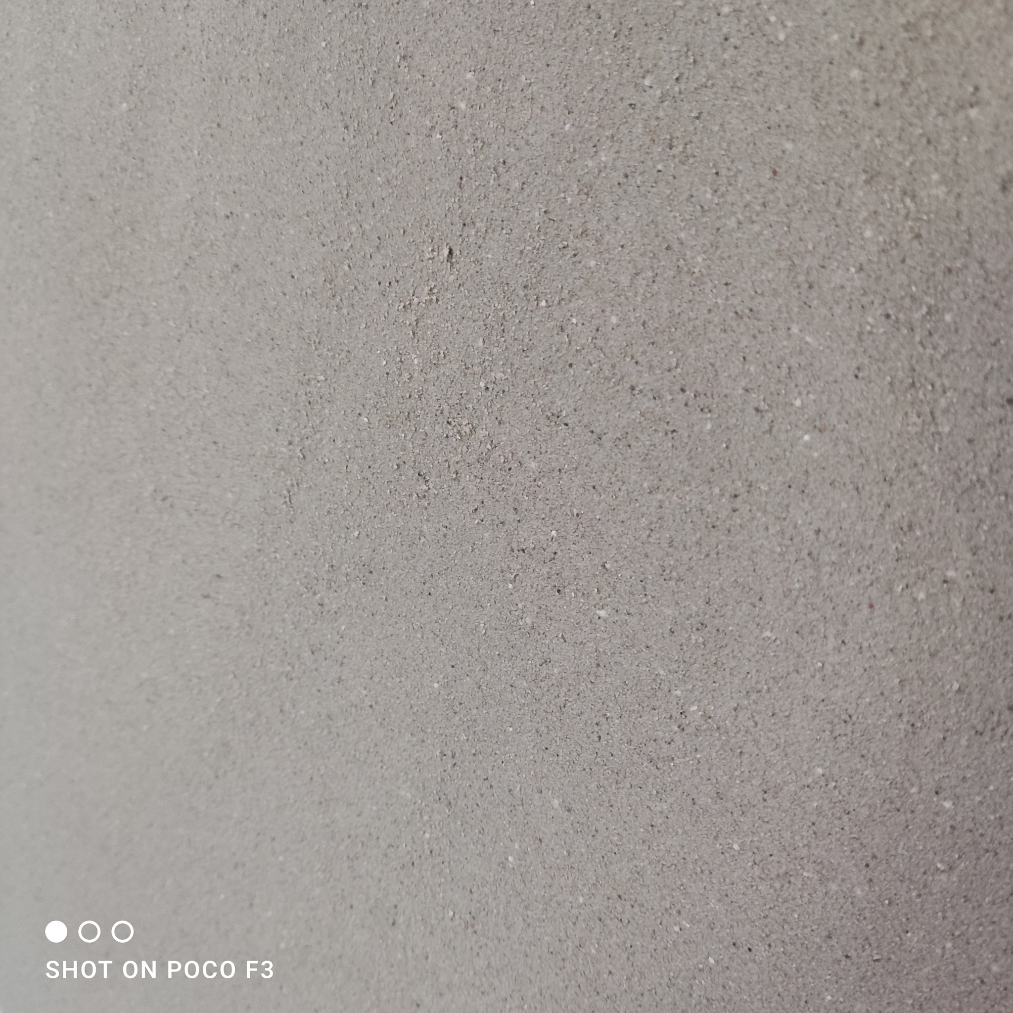Szara, chropowata powierzchnia ściany z bliska, widoczne drobne nierówności i ziarna, sfotografowana telefonem Poco F3.