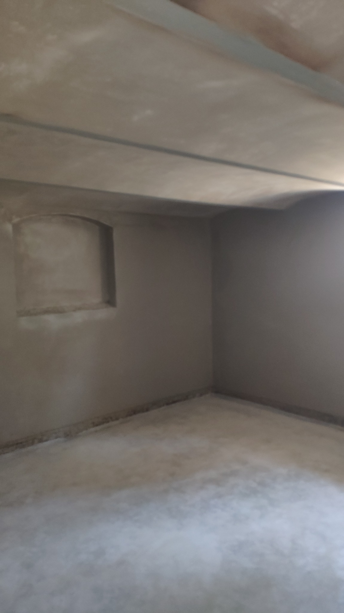 Surowe wnętrze piwnicy po nałożeniu gładzi cementowej na ściany i sufit, widoczna wnęka w ścianie, metalowe profile pod sufitem.