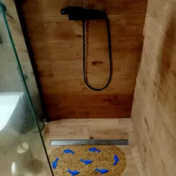 Ukończona łazienka z kabiną prysznicową, drewnopodobnymi płytkami na ścianach i podłodze oraz czarną armaturą. Na podłodze leży okrągły dywanik z motywem niebieskich delfinów.