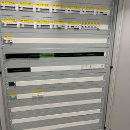 Kma Energy - Rozdzielnica elektryczna z zamontowanymi zabezpieczeniami, wyłącznikami, ogranicznikiem przepięć i licznikiem Loxone, widok z bliska na szare panele i elementy instalacji elektrycznej.