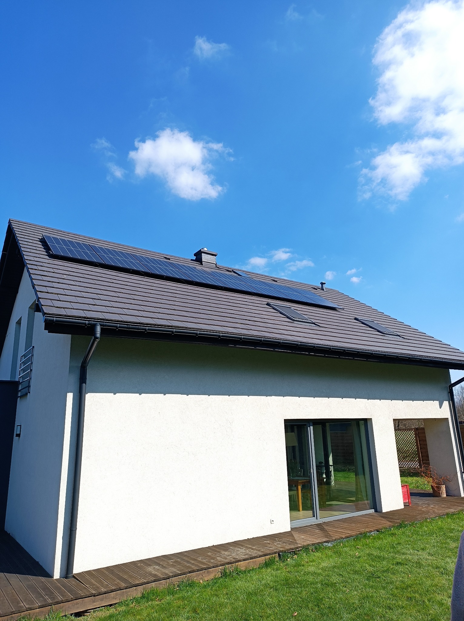 Panele słoneczne zamontowane na dachu nowoczesnego domu jednorodzinnego z brązową dachówką i białymi ścianami w słoneczny dzień.