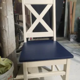 Biało-granatowe krzesło z krzyżowym oparciem, widoczne w warsztacie obok wiadra i roweru.