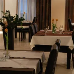 Elegancko nakryte stoły w restauracji z ciemnymi drewnianymi krzesłami, białymi obrusami z brązowymi bieżnikami i pomarańczowymi tulipanami w wazonach na każdym stole.