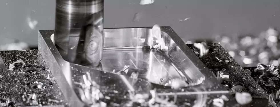 Frezarka CNC w trakcie obróbki metalowego elementu, wióry w powietrzu, widoczne detale frezu i obrabianego przedmiotu.