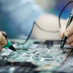 Dłonie technika z precyzyjnymi sondami mierniczymi diagnozują płytę główną laptopa, widoczne elementy elektroniczne i ścieżki obwodu drukowanego.