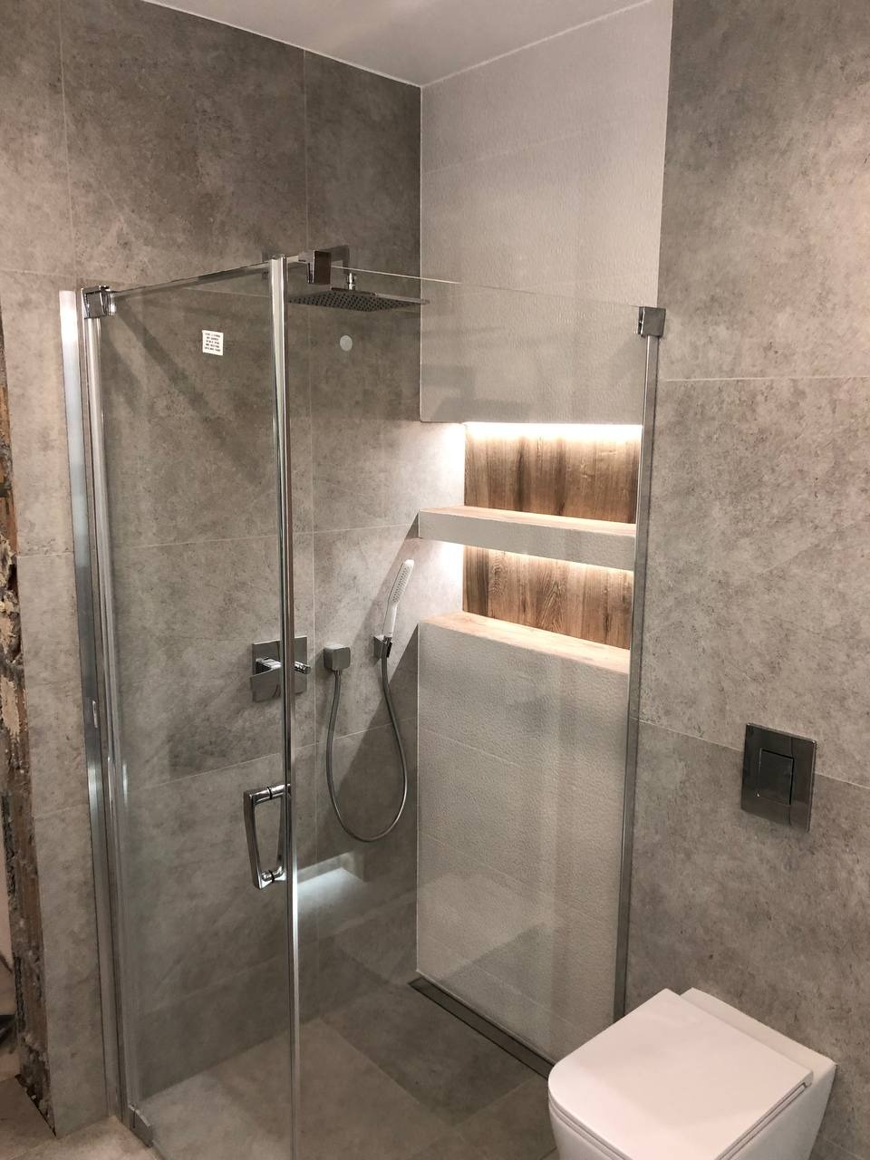 Nowoczesna kabina prysznicowa z grafitowymi płytkami, półkami z podświetleniem LED i odpływem liniowym w wyremontowanej łazience.
