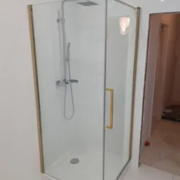 Nowoczesna kabina prysznicowa z chromowaną armaturą i złotymi profilami, widoczna na tle białych płytek w łazience w trakcie remontu.