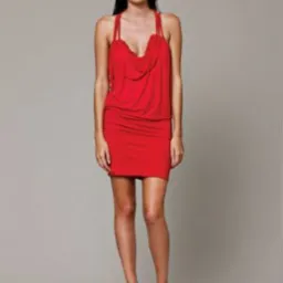 Kobieta w czerwonej, drapowanej sukience mini z podwójnymi ramiączkami i beżowych botkach na obcasie na neutralnym tle.