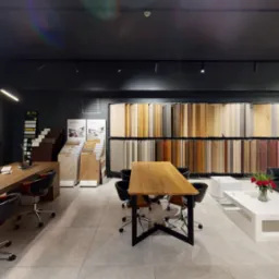 Salon z ekspozycją paneli podłogowych i parkietów, z długim drewnianym stołem, sofą i dekoracją z mchu na ścianie.